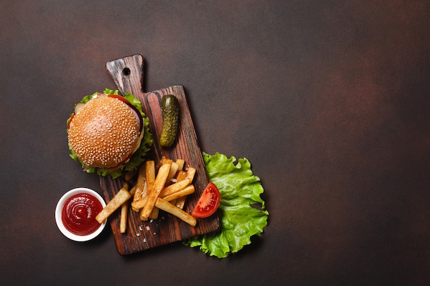 Selbst gemachter hamburger mit bestandteilen rindfleisch, tomaten, kopfsalat, käse, zwiebel, gurken und pommes-frites auf schneidebrett Premium Fotos