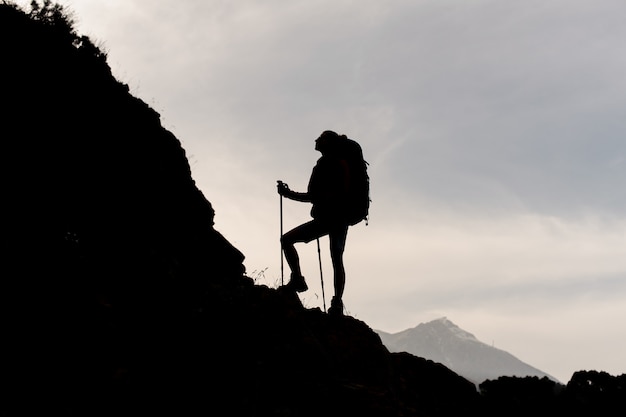 Silhouettieren sie die frau, die auf den felsen mit dem wandern des rucksacks und der spazierstöcke steht Premium Fotos