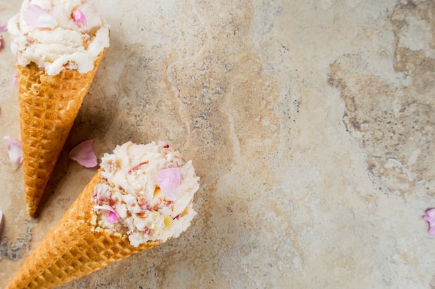 Sommer erfrischende desserts. vegane diätkost. eiscreme mit den rosafarbenen blumenblättern und den scheiben der mandel, in den klassischen waffeleiscremekegeln, auf einer beige hellen konkreten tabelle. copyspace draufsicht Premium Fotos