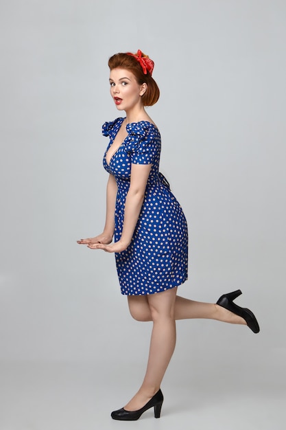Stereotypes bild des emotionalen lustigen pin-up-mädchens in stilvollem  vintage-outfit mit erstauntem gesichtsausdruck, mundöffnung, koketter geste  und beinheben hinten | Kostenlose Foto