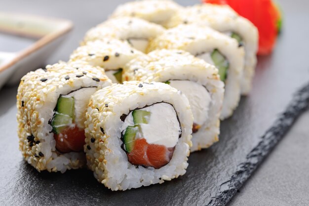 Sushi-rolle mit lachs, philadelphia-käse und sesam auf teller nah oben ...