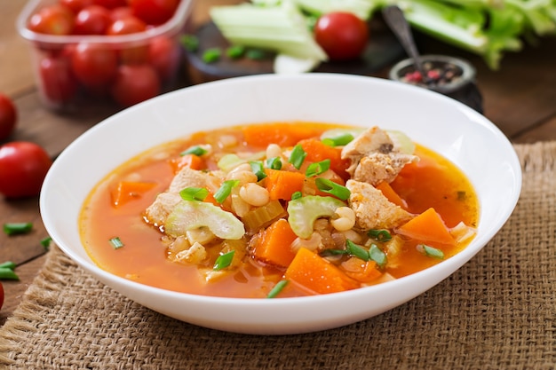 Tomaten-Hühnersuppe mit Kürbis, Bohnen und Sellerie in weißer Schüssel