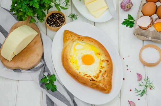 Traditionelles georgisches käsegebäck ajarian khachapuri mit eiern und butter auf einer platte auf einer weißen holzoberfläche Premium Fotos