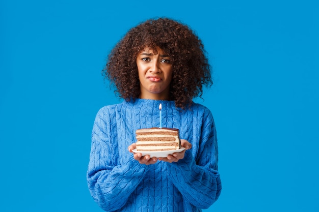 Trauriges Und Dusteres Depressives Susses Afroamerikanisches Madchen Das Sich An Ihrem Geburtstag Einsam Fuhlte Niemand Kam Party Hielt Kuchen Mit Einer Einzelnen Brennenden Kerze Schmollte Und Stand Uber Blauer Wand Premium Foto