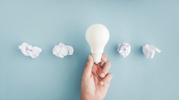 Übergeben sie das halten der weißen glühlampe mit zerknitterten papierbällen auf grauem hintergrund Kostenlose Fotos