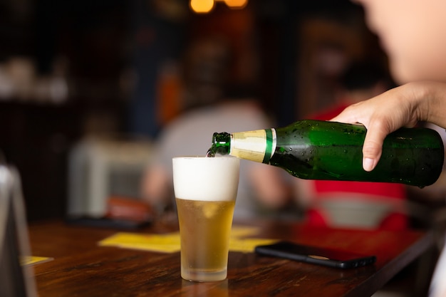 Übergeben sie strömendes bier von der flasche in ein glas im unschärfehintergrund. Premium Fotos