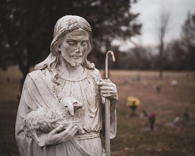 Verwitterte Statue Von Jesus Christus Mit Einem Schaf In Seinen Handen Auf Einem Unscharfen Hintergrund Kostenlose Foto