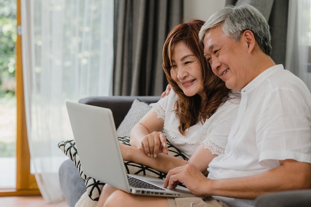 Videoanruf der asiatischen älteren paare zu hause. asiatische ältere chinesische großeltern, unter verwendung des laptopvideoanrufs, der mit familienenkelkind spricht, scherzt beim auf sofa im konzept des wohnzimmers zu hause liegen. Kostenlose Fotos