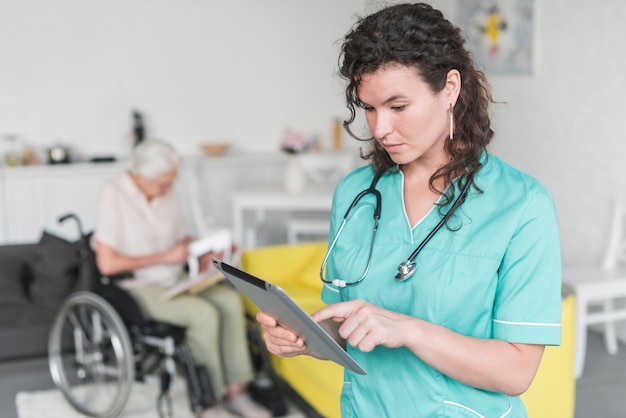 Weibliche krankenschwester, welche die digitale tablette steht vor der älteren frau sitzt auf rollstuhl verwendet Kostenlose Fotos