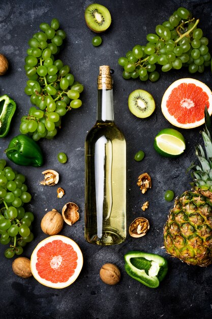 Wein-konzept. flasche und glas junger weißer biowein mit grünen trauben, pampelmuse und anderer frucht auf einem grauen steinhintergrund Premium Fotos