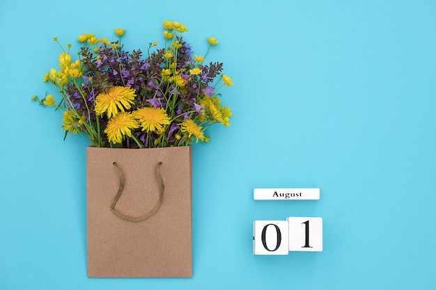 Würfelkalender 1. august und bunte rustikale blumen des feldes im handwerkspaket auf blauem hintergrund Premium Fotos