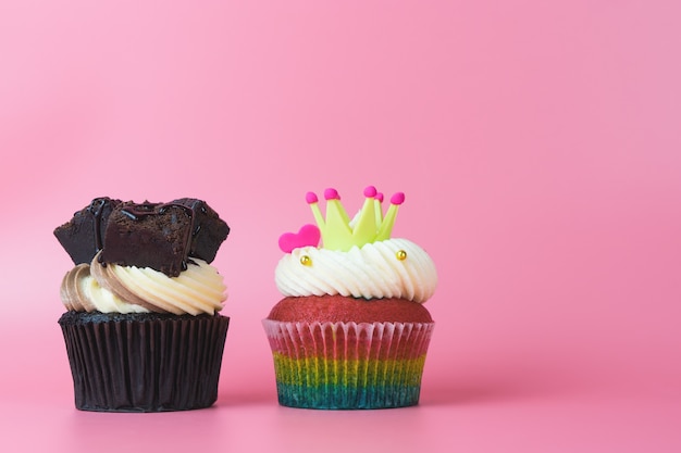 プレミアム写真 2カップケーキチョコレートと虹のカップケーキピンクの背景にコピースペース