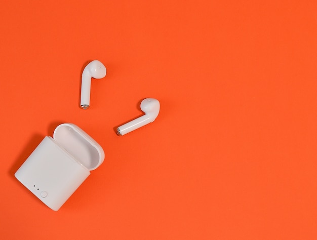 2 white wireless earphones in-ear with bluetooth on an orange wall.copy space. flat lay Premium Phot