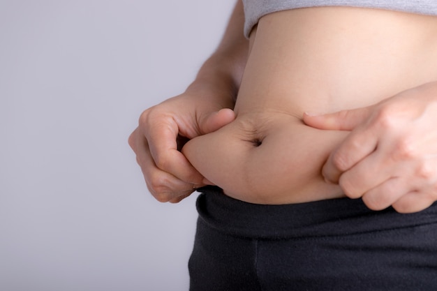 過剰な腹脂肪を持っている太った女性の手。女性のダイエットライフスタイルコンセプトは、腹を減らし、健康な胃の筋肉を形作ります。 Premium写真