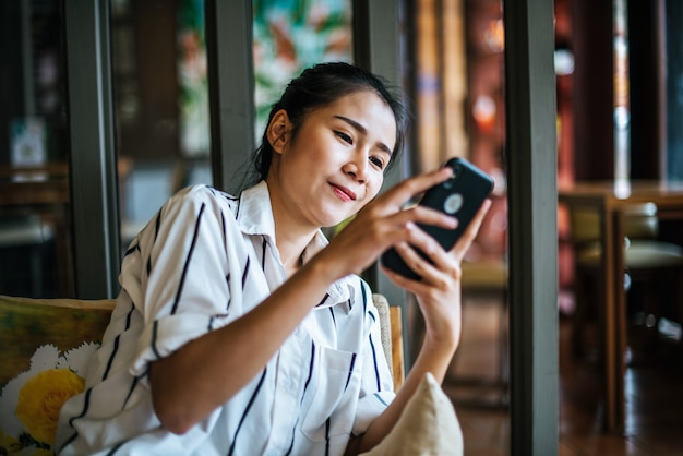 女性が座っているとカフェで彼女のスマートフォンをプレイ 無料写真