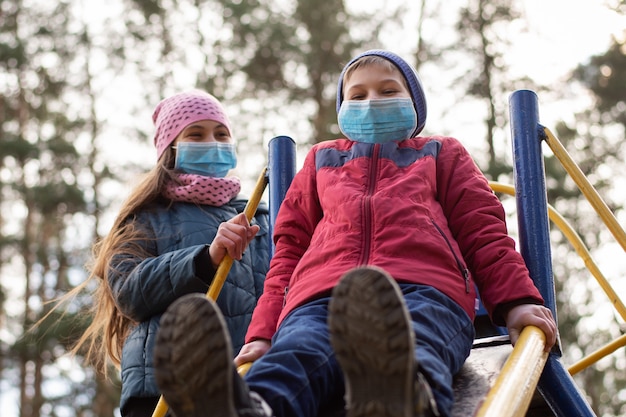 Дети в медицинских масках на детской площадке на открытом воздухе ...