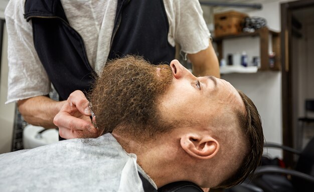 Master Barber Delaet Prichesku I Ukladku Koncepciya Dlya Parikmaherskih Ukladka Borody I Strizhka Ukladka Chernoj Borody Tak Modno I Stilno Reklamno Parikmaherskaya Koncepciya Premium Foto