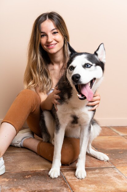 室内の床に座っている彼女のハスキー犬を持つ若いきれいな女性 プレミアム写真