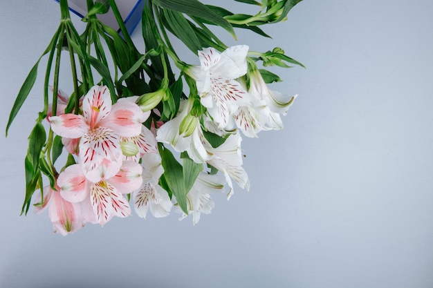 明るい灰色の背景に青いボックスにピンクと白の色のアルストロメリアの花の花束の側面図 無料の写真