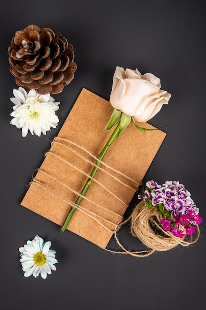 茶色の紙のグリーティングカードと白い色のバラのトップビューはロープで縛られ デイジーの花と円錐形のトルコのカーネーションが黒いテーブルに 無料の写真