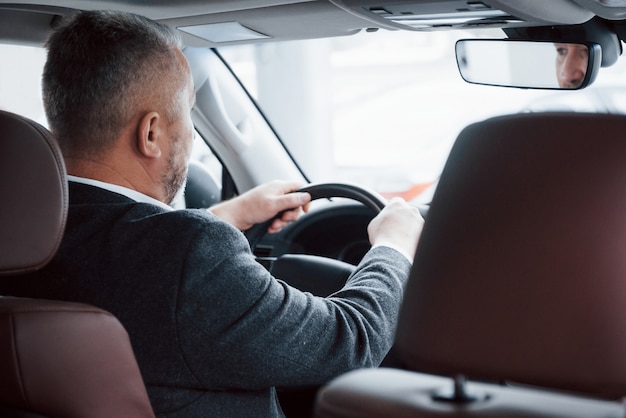 会議に行きます 現代の新しい車を運転する公式の服の上級ビジネスマンの後ろからの眺め 無料の写真