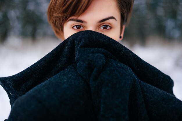 天使のような美しい顔を持つ素敵な女の子 雪に覆われた冬の森で凍った女性と暖かい服装 探している感情的な女性の目 プレミアム写真