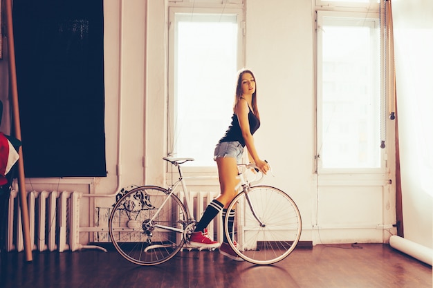 屋内のアパートでポーズをとって白いレトロな自転車の若い女性 プレミアム写真