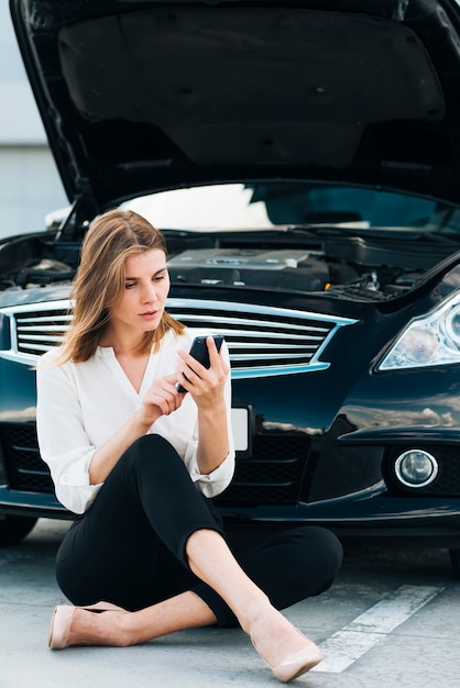 女性は彼女の電話と黒い車をチェック 無料の写真