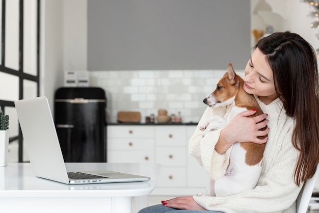 ノートパソコンを見ながら彼女の犬を保持している女性の側面図 無料の写真