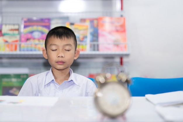 かわいいアジアの子供の学生はぼんやりした時計と本を白い背景に瞑想 プレミアム写真