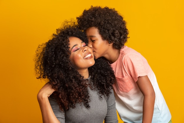幼児の息子を持つ若いアフリカ系アメリカ人の母の肖像画 息子が母親にキスします 黄色の壁 ブラジルの家族 プレミアム写真