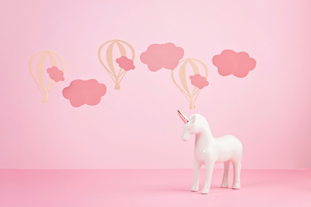 雲と風船とピンクのパステル調の背景の上のかわいい白いユニコーン