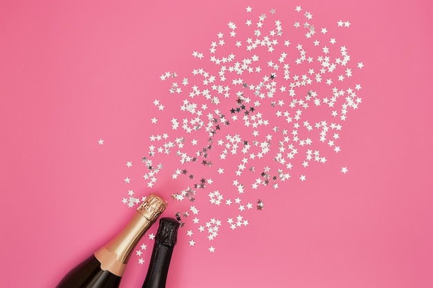 ピンクの背景に紙吹雪とシャンパンのボトル。 Premium写真