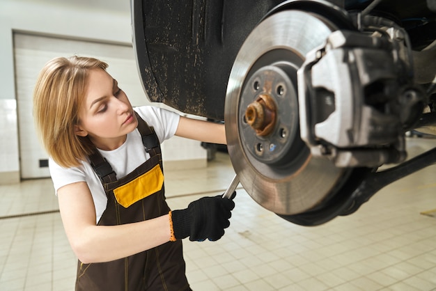 ツールを使用して車のブレーキディスクを修正するつなぎ服の女の子 無料の写真