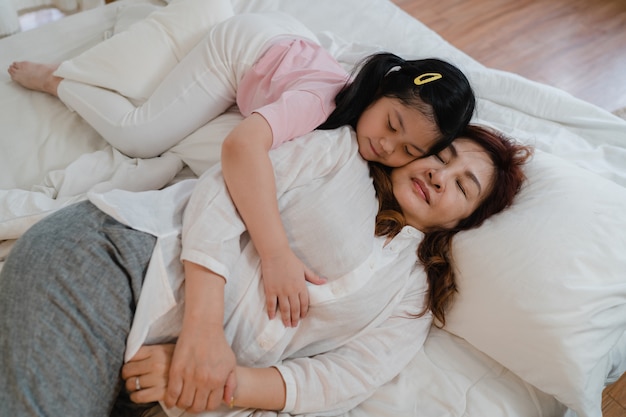 アジアの祖母は家で寝ています シニア中国人 おばあちゃんは 夜のコンセプトで自宅の寝室のベッドに横になって目を覚ますための頬にキス若い孫娘の女の子とリラックスします 無料の写真