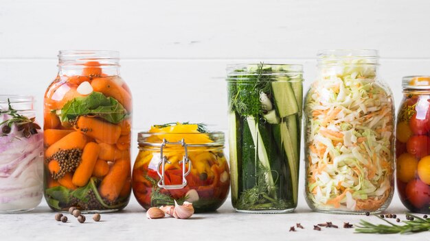 野菜の漬物 長期保存のためにガラス瓶にさまざまな野菜を塩漬けします ガラスの瓶に野菜を保存します さまざまなテーブルの上の緑の野菜を発酵させた プレミアム写真