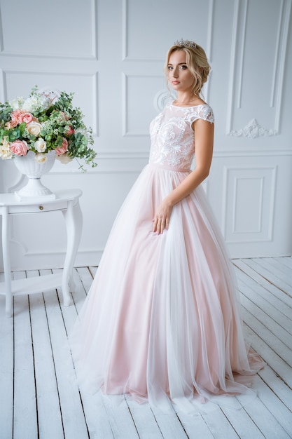 髪とメイクの美しい花嫁は 花で明るい装飾の繊細なピンクのウェディングドレスに立っています 無料の写真