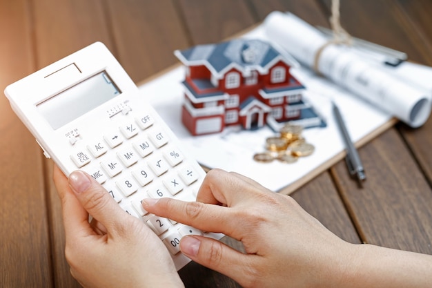 A female hand operating a calculator in front of a Villa house model Free Photo