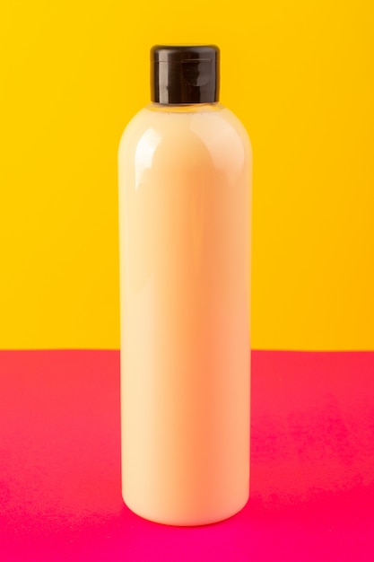 正面図のクリーム色のボトルのプラスチックシャンプー缶ピンクイエローバックグラウンド化粧品美容髪に分離された黒のキャップ 無料の写真