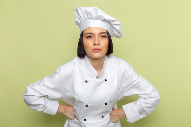 白いクックスーツと緑の壁の女性ポーズ食品料理色でポーズキャップで正面の若い女性クック 無料の写真