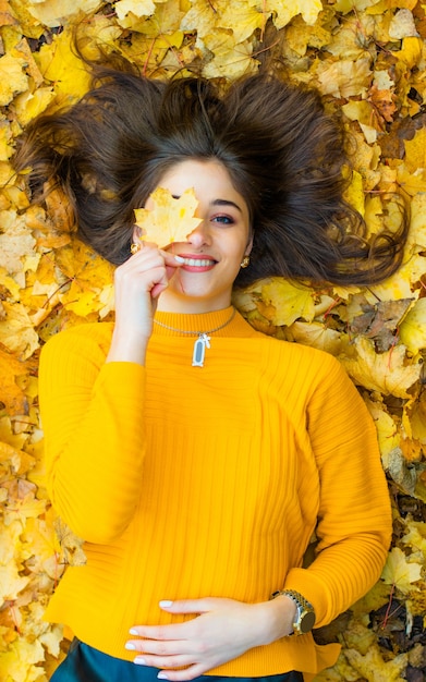 紅葉の上に横たわる黄色いタートルネックの女の子が目を葉で覆っている プレミアム写真