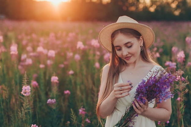 花束を持った幸せな女の子が花の牧草地を歩きます 愛と春の開花 プレミアム写真