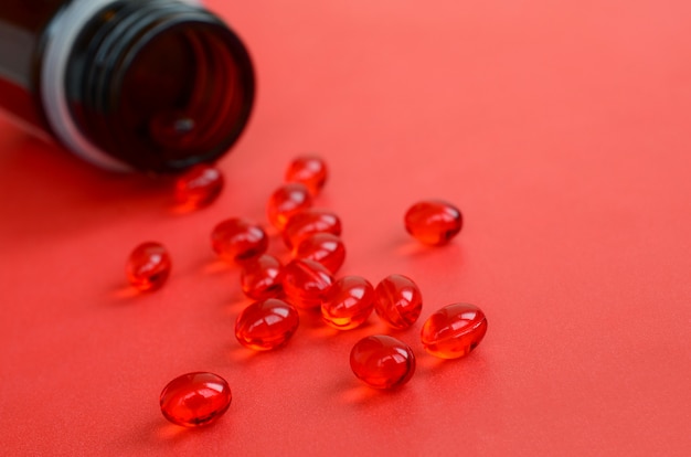 たくさんの透明な赤い錠剤が小さなガラスの茶色の瓶から赤い表面に散らばっていました プレミアム写真