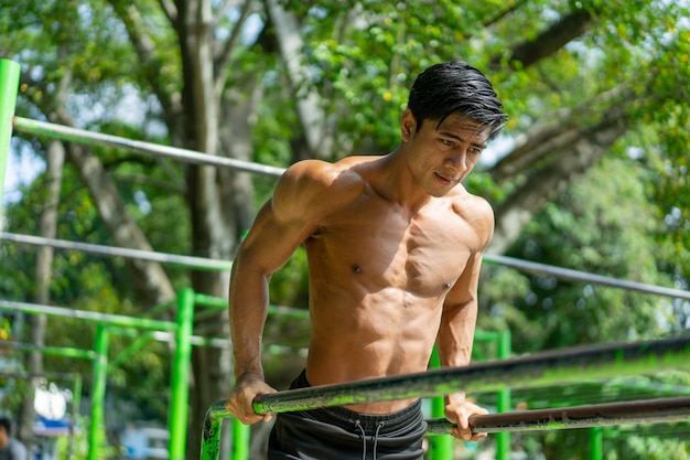 公園で屋外で運動しながら上腕二頭筋と上腕三頭筋を鍛えるために懸垂をする筋肉質の男性 プレミアム写真