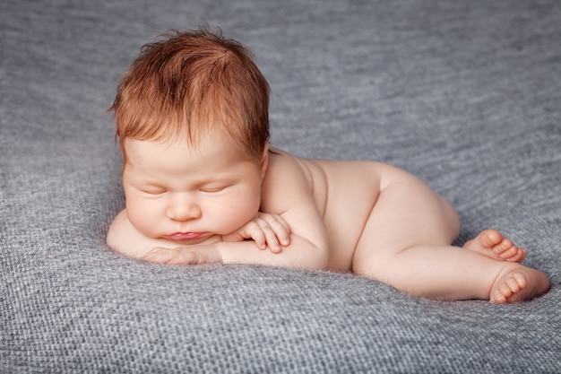 裸の生まれたばかりの赤ちゃんが丸くなり 灰色の織り目加工の毛布の上で眠っています プレミアム写真