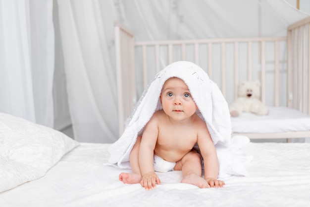 入浴後おむつの明るい保育園で白いベッドの上のタオルに生後6ヶ月の女の子の小さな子供 プレミアム写真