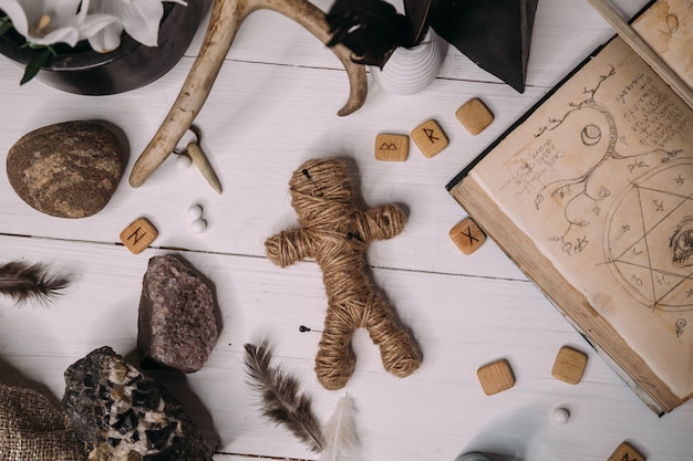 ロープでできたブードゥー教の人形は 古い本のグリモワールにあり 魔法の儀式のオブジェクトに囲まれています プレミアム写真