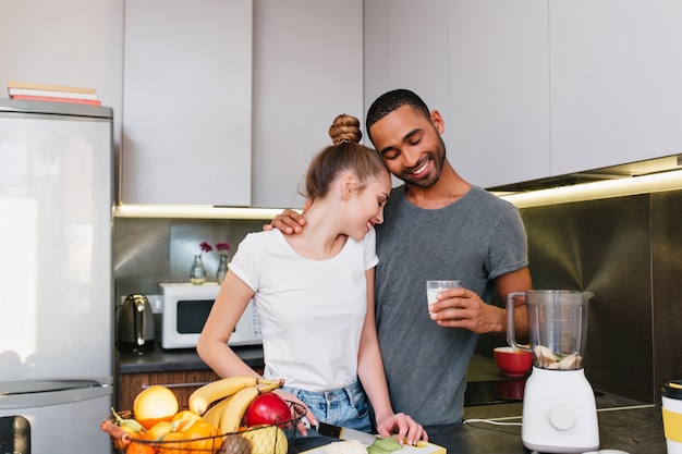 キッチンで朝食を作る若いカップル Tシャツを着た男女が抱き合って 一緒に料理をし 幸せそうな顔で抱き合うカップル 無料の写真