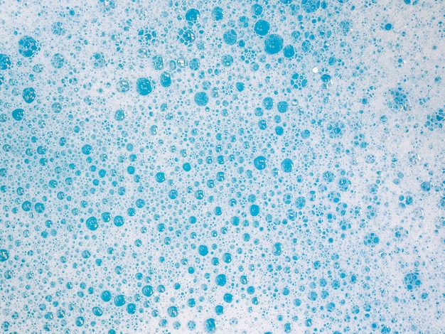 服を洗う青いお風呂で水面に洗剤の泡と抽象的な背景 プレミアム写真