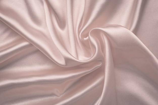 シルクの抽象的な背景。柔らかいピンクの光沢のある生地。繊細なバラの布のテクスチャ。サテンの折り目、波のパターン。曲線のあるパステル調の絹のような背景、高級ファッション。  | プレミアム写真